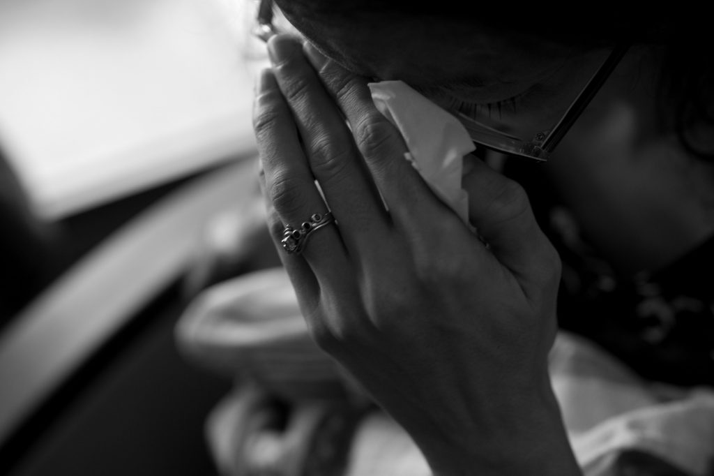 Woman holding her hand to her face, crying into a tissue.