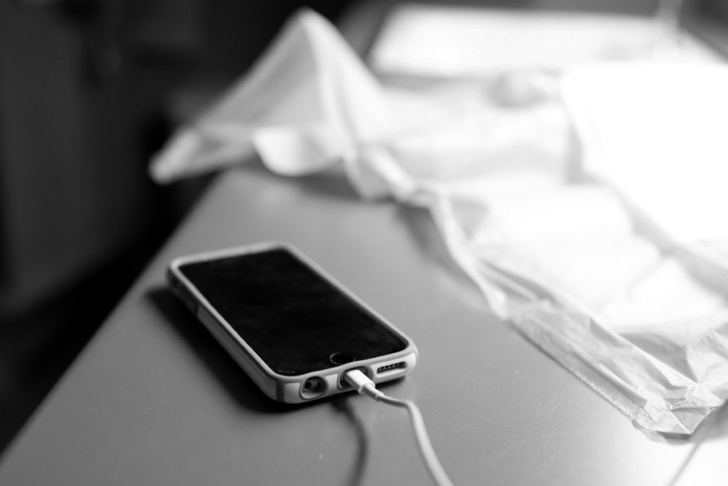 An iphone is plugged into a socket and sits on a hospital room table. 