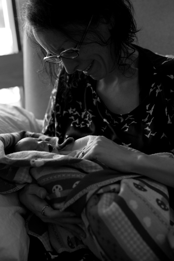 A woman holds a still born baby girl in her arms. She is crying and trying to get the baby's hand inside her blanket. 