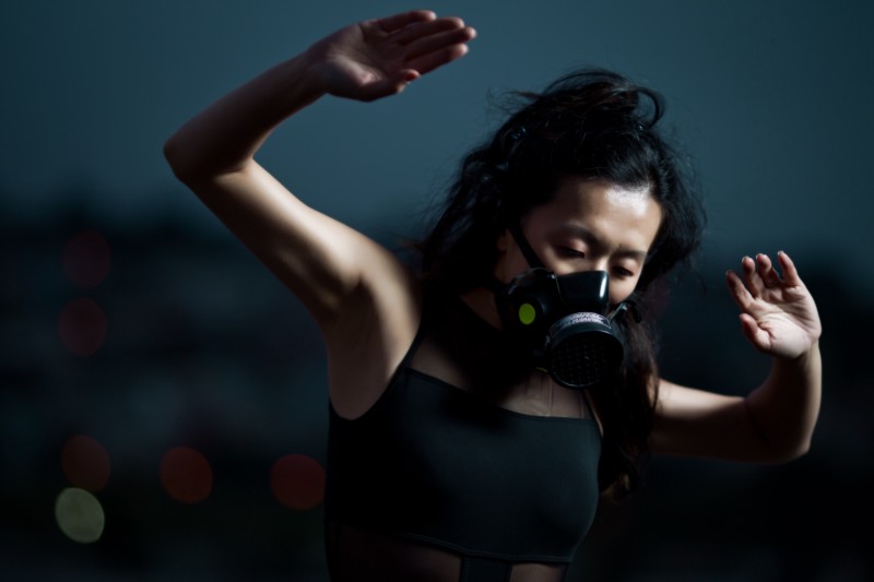 A ballerina, surrounded by dark clouds, has her hands in the air. She is wearing a gas mask. 