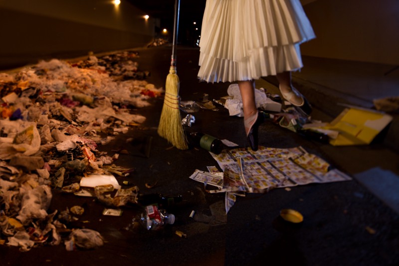 A close up of a ballerina's feet and the bottom of her white dress, while she sweeps garbage into a pile.